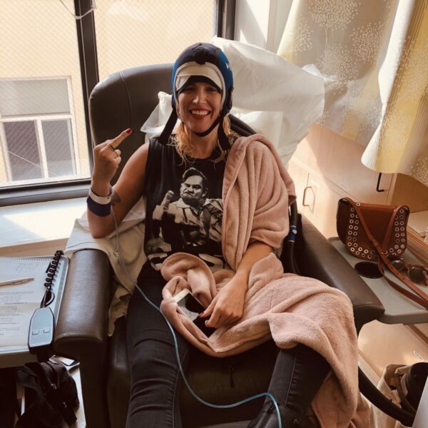 Marisa Sullivan smiles in a chemo chair as she holds up her middle finger to cancer